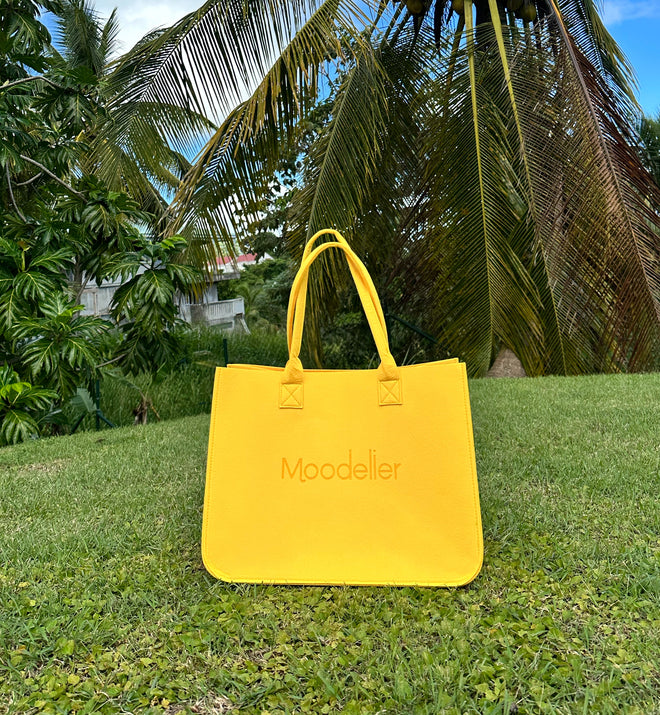 A Moodelier Tote bag in Sunflower color with a palm trees background.